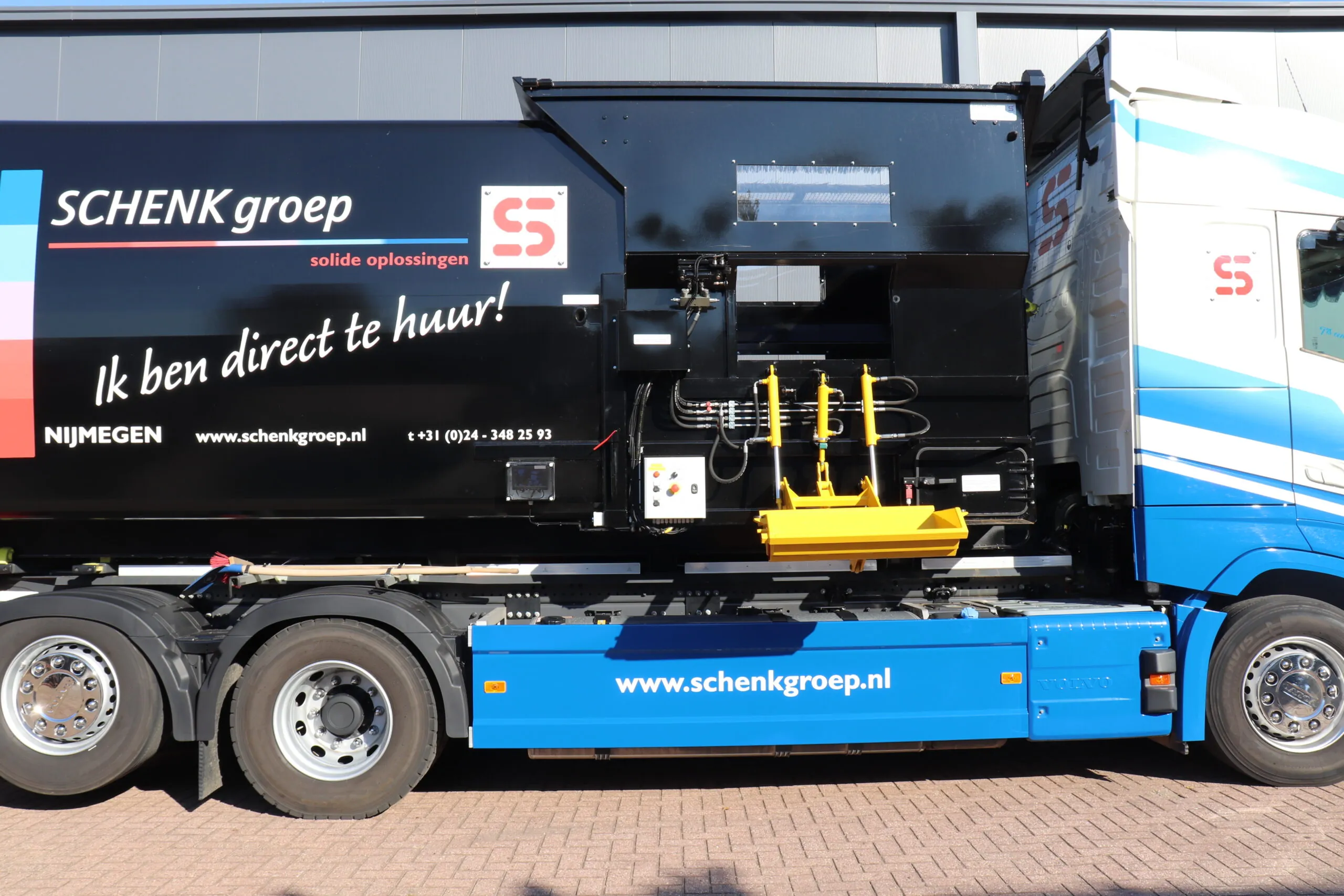 Hydraulische belader met gele arm en zwarte behuizing op een afvalinzameltruck van SCHENK Groep, inclusief website en telefoonnummer
